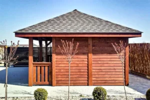 Altana A19 to elegancka i funkcjonalna konstrukcja, która doskonale łączy przestrzeń wypoczynkową z praktycznym domkiem, idealnym do przechowywania lub dodatkowego użytku. Całkowity wymiar altany wynosi 6,00m x 4,00m, z czego altana zajmuje 4,40m x 4,00m, a domek 1,60m x 3,00m. Przed domkiem znajduje się uroczy tarasik o wymiarach 1,60m x 1,00m, który stanowi doskonałe miejsce na relaks.